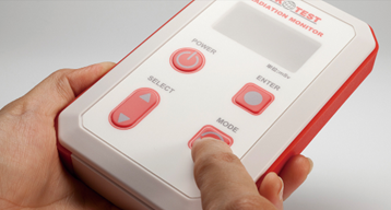 Handheld insulation-monitor test unit with a red and white membrane keypad, held in one hand